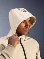 Alpinestars Radium Tech Hoodie in Mastic Aluminum, primo piano di un uomo con il cappuccio sollevato, logo Alpinestars sulla parte superiore, giacca da moto urbana con guscio tecnico antivento, estetica streetwear moderna per la guida in città