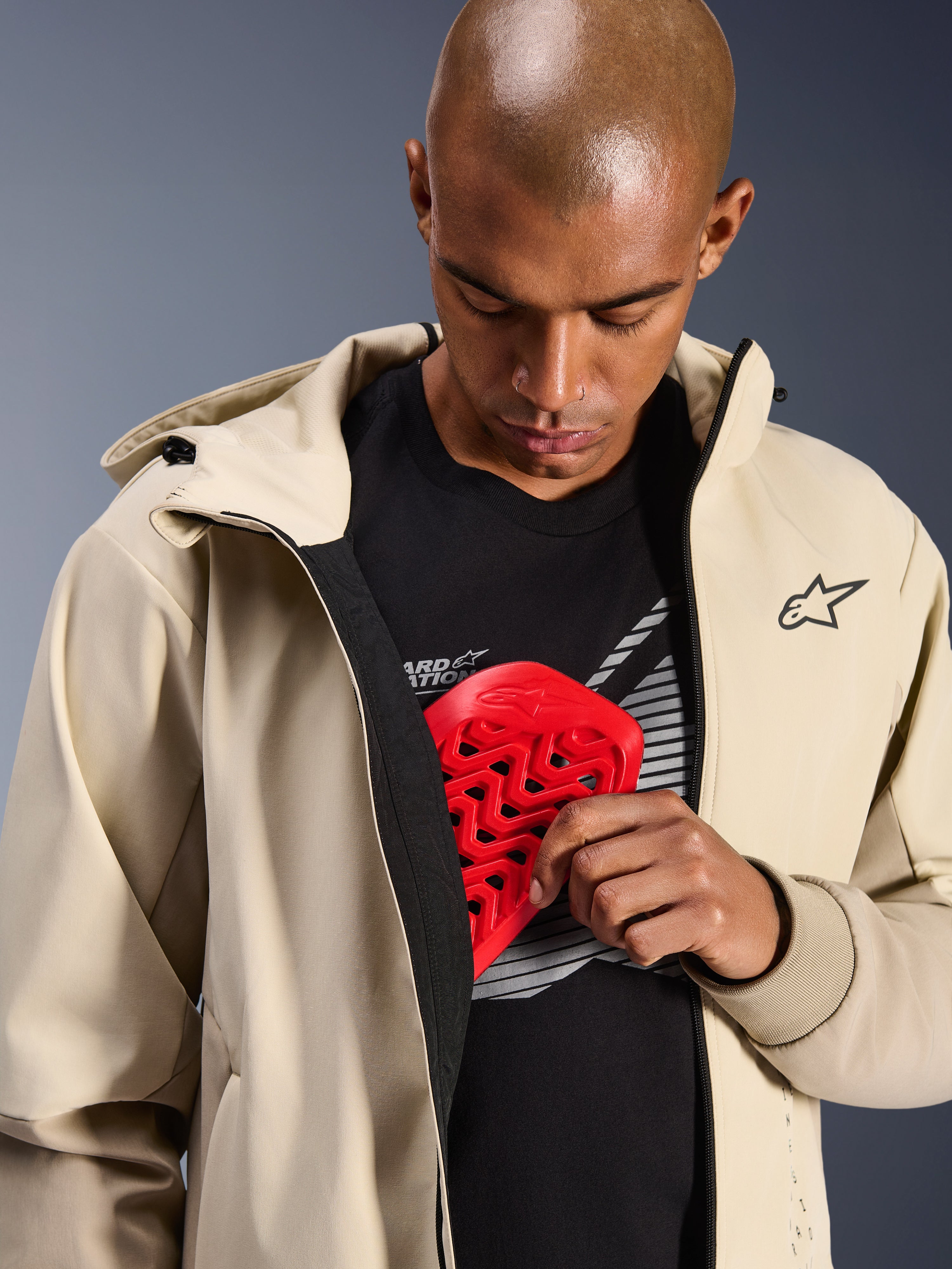 Alpinestars Radium Tech Hoodie in Mastic Aluminum, giacca da moto urbana, modello che mostra la tasca interna per le protezioni con un paratorace Nucleon rosso, guscio tecnico antivento con design casual a felpa con cappuccio e marchio Alpinestars.