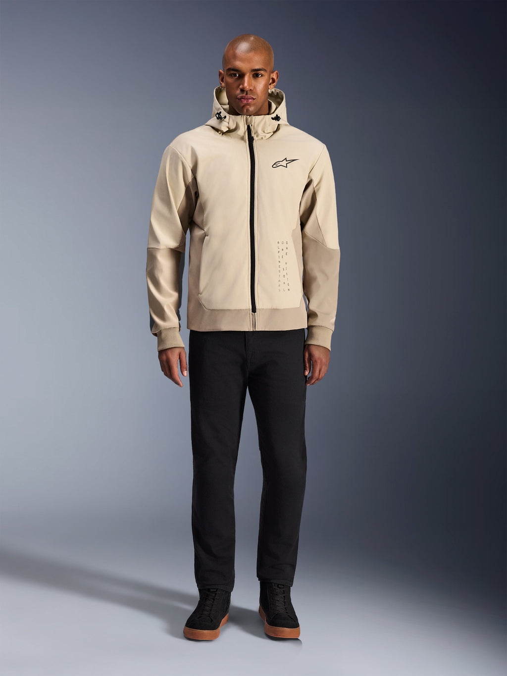 Alpinestars Radium Tech Hoodie in Mastic Aluminum, felpa da moto urbana indossata da un modello con pantaloni neri e stivali neri, caratterizzata da una cerniera nera a tutta lunghezza, un piccolo logo sul petto e una vestibilità atletica per la guida in città.