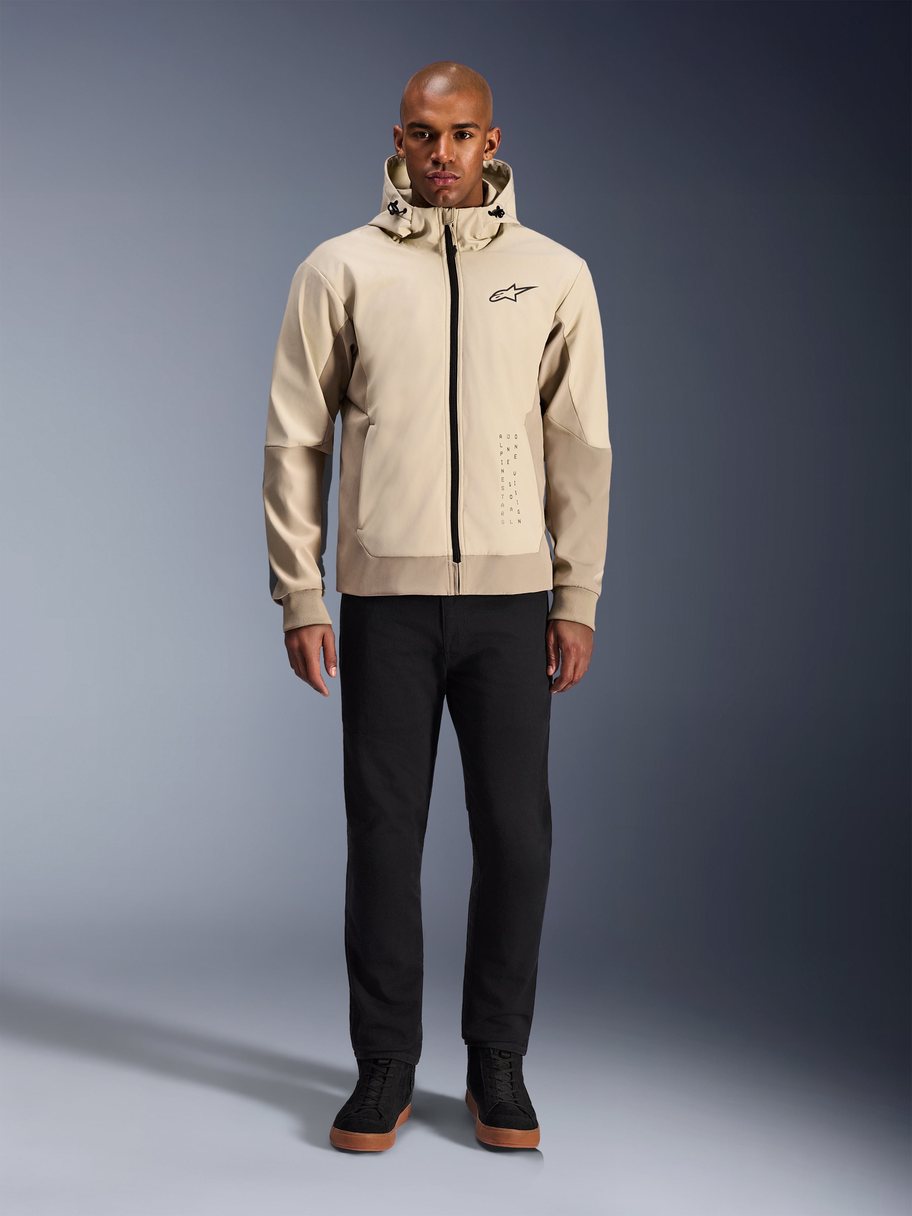 Alpinestars Radium Tech Hoodie in Mastic Aluminum, felpa da moto urbana indossata da un modello con pantaloni neri e stivali neri, caratterizzata da una cerniera nera a tutta lunghezza, un piccolo logo sul petto e una vestibilità atletica per la guida in città.