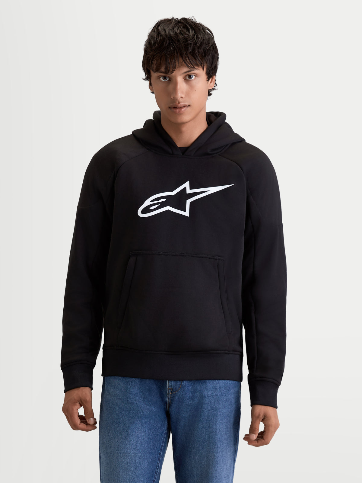 Alpinestars Felpa Con Cappuccio Ageless, felpa da moto urbana da uomo, colore nero con logo bianco sul petto, tasca a marsupio frontale e struttura in tessuto casual, vista frontale su un modello