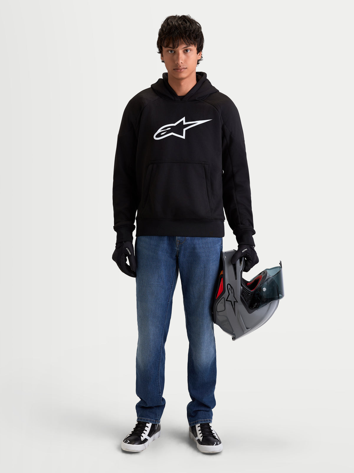 Alpinestars Felpa Con Cappuccio Ageless, felpa da moto urbana da uomo in nero con logo Astar bianco sul petto, indossata da un modello con guanti da moto e casco
