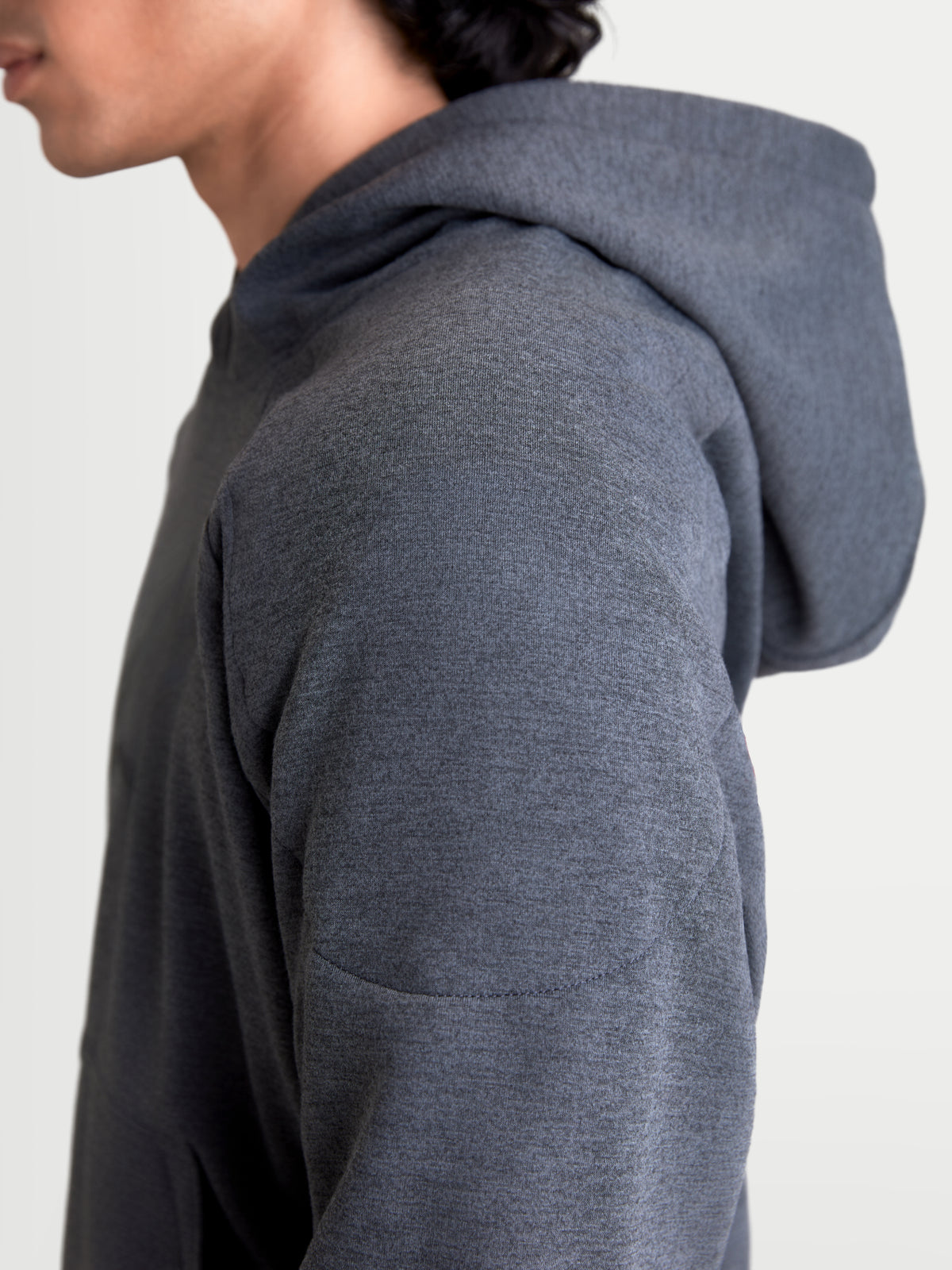 Alpinestars Felpa Con Cappuccio Ageless, felpa da moto urbana da uomo, grigio asfalto melange, vista ravvicinata del profilo laterale con dettagli della costruzione in tessuto a maglia e rinforzo sulla spalla indossata da un modello