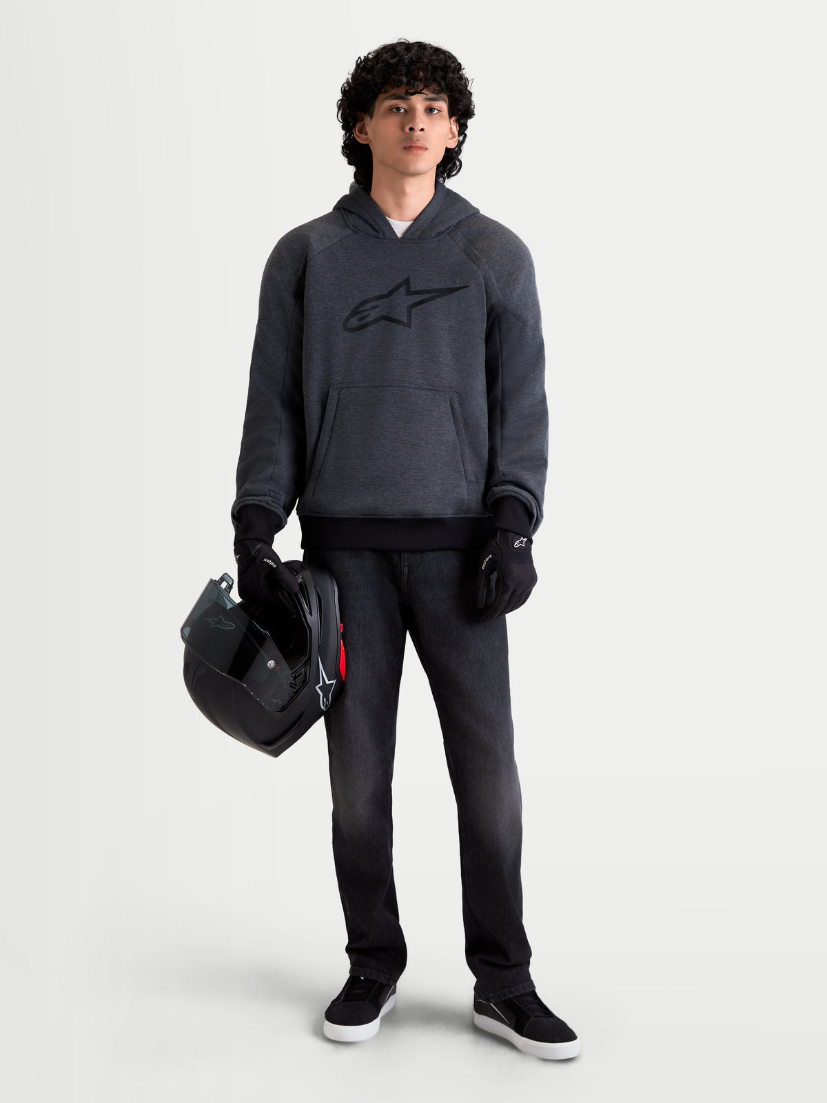 Alpinestars Felpa Con Cappuccio Ageless, felpa da moto urbana da uomo, grigio scuro melange, vista frontale su un modello che indossa guanti da moto neri e tiene un casco