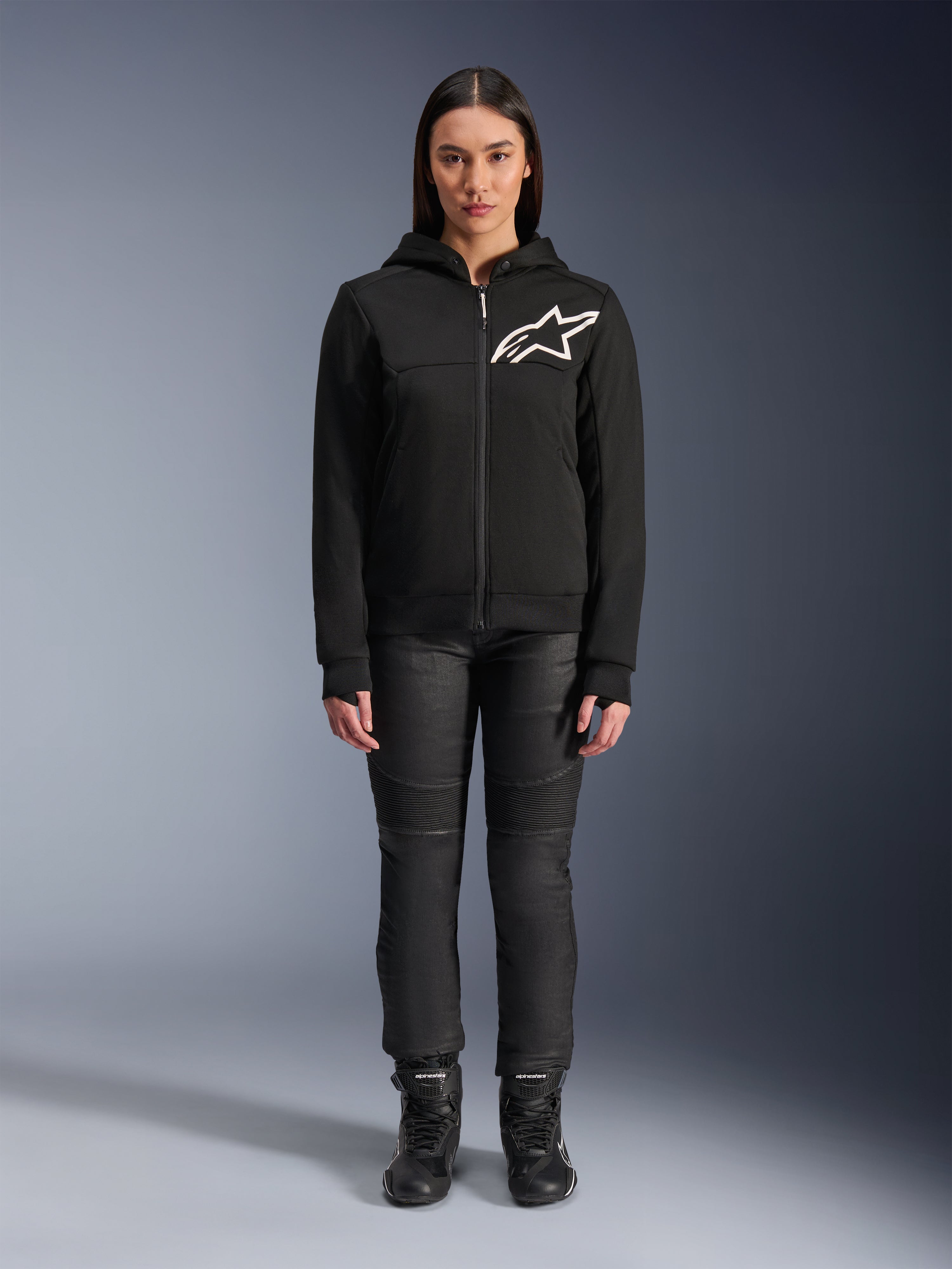 Alpinestars Stella Chrome V2 Sport Hoodie da donna, nera con logo Astars bianco sul petto, abbinata a pantaloni tecnici da guida e stivali neri, design di abbigliamento moto urbano