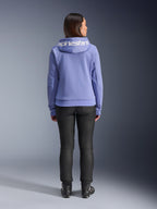 Alpinestars Stella Chrome V2 Sport Hoodie, blu violetto, vista posteriore di una donna che indossa la felpa con logo Alpinestars bianco sul cappuccio, abbinata a pantaloni neri e stivali da moto, abbigliamento casual da moto urbano