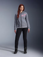 Alpinestars Stella Chrome V2 Sport Hoodie, felpa da moto con cappuccio, grigio melange e rosa fluo, indossata da una donna con pantaloni neri e stivali, logo a stella Alpinestars rosa sul petto, pile tecnico leggero con vestibilità atletica casual