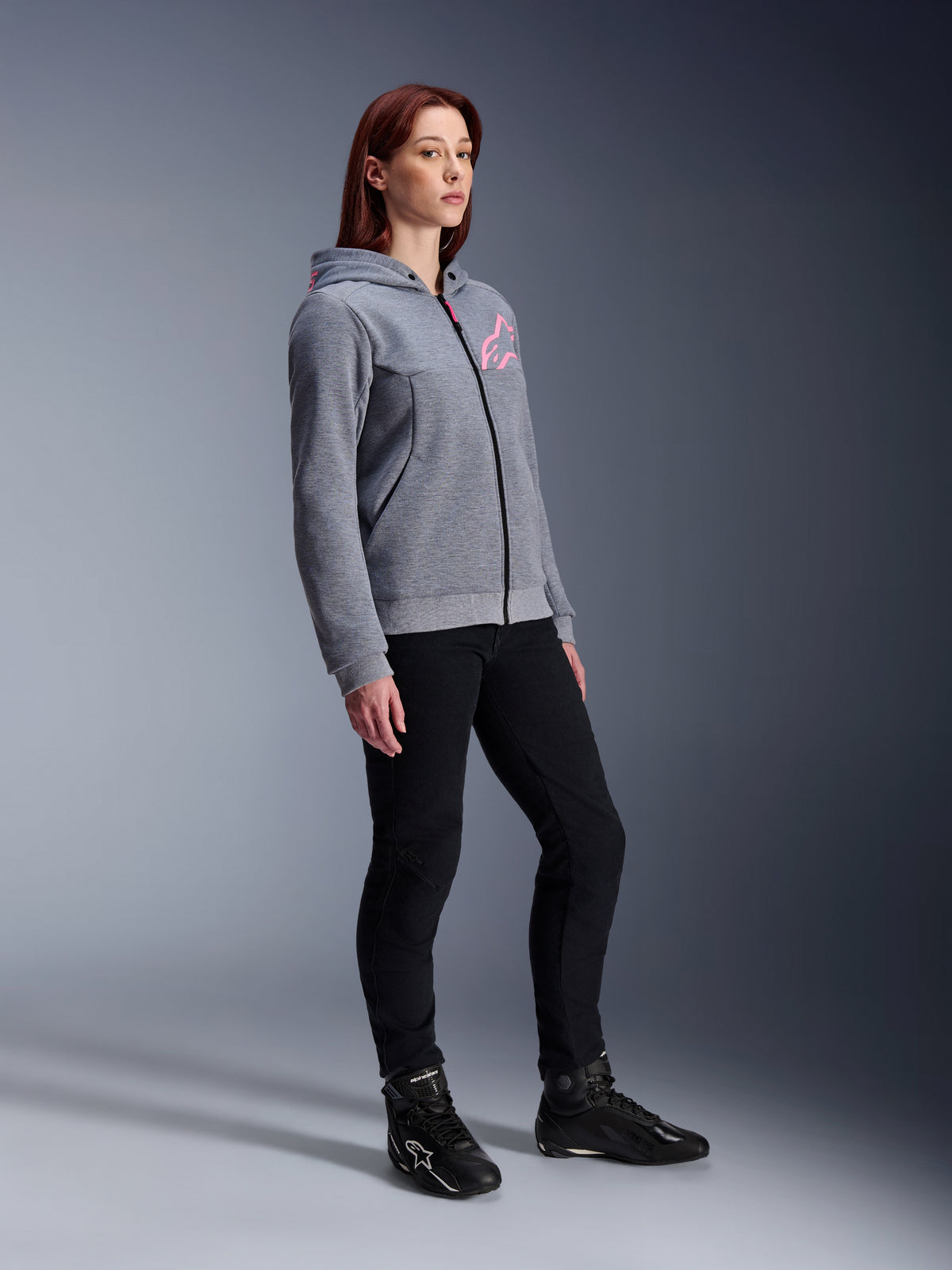 Alpinestars Stella Chrome V2 Sport Hoodie, felpa da moto da donna, grigio melange e rosa fluo, indossata con pantaloni da moto neri e stivali neri, abbigliamento casual per guida urbana