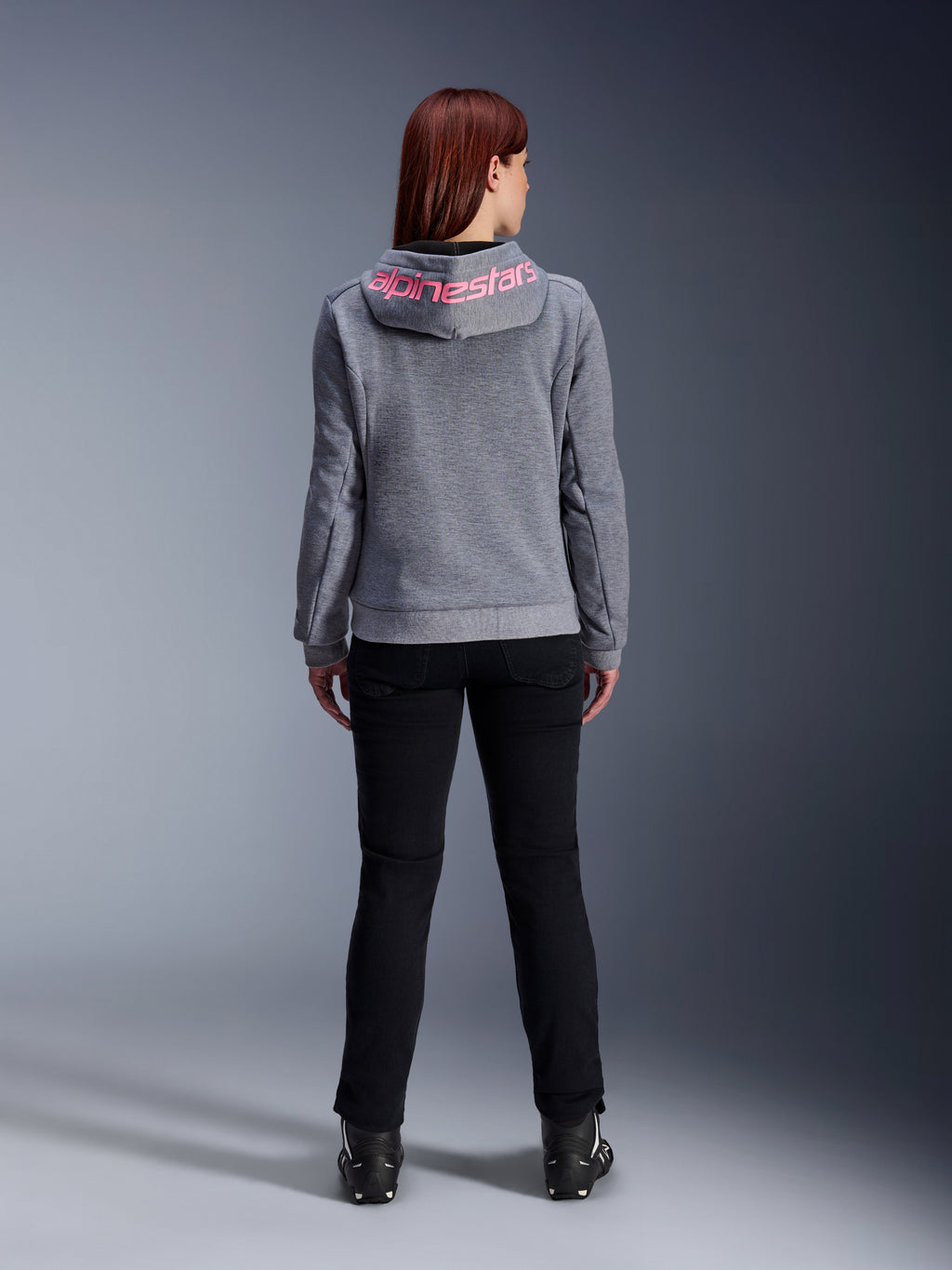 Alpinestars Stella Chrome V2 Sport Hoodie, felpa da moto da donna, grigio mélange e rosa fluo, vista posteriore con logo Alpinestars rosa sul cappuccio, indossata con pantaloni da guida e stivali neri, abbigliamento moto casual da donna