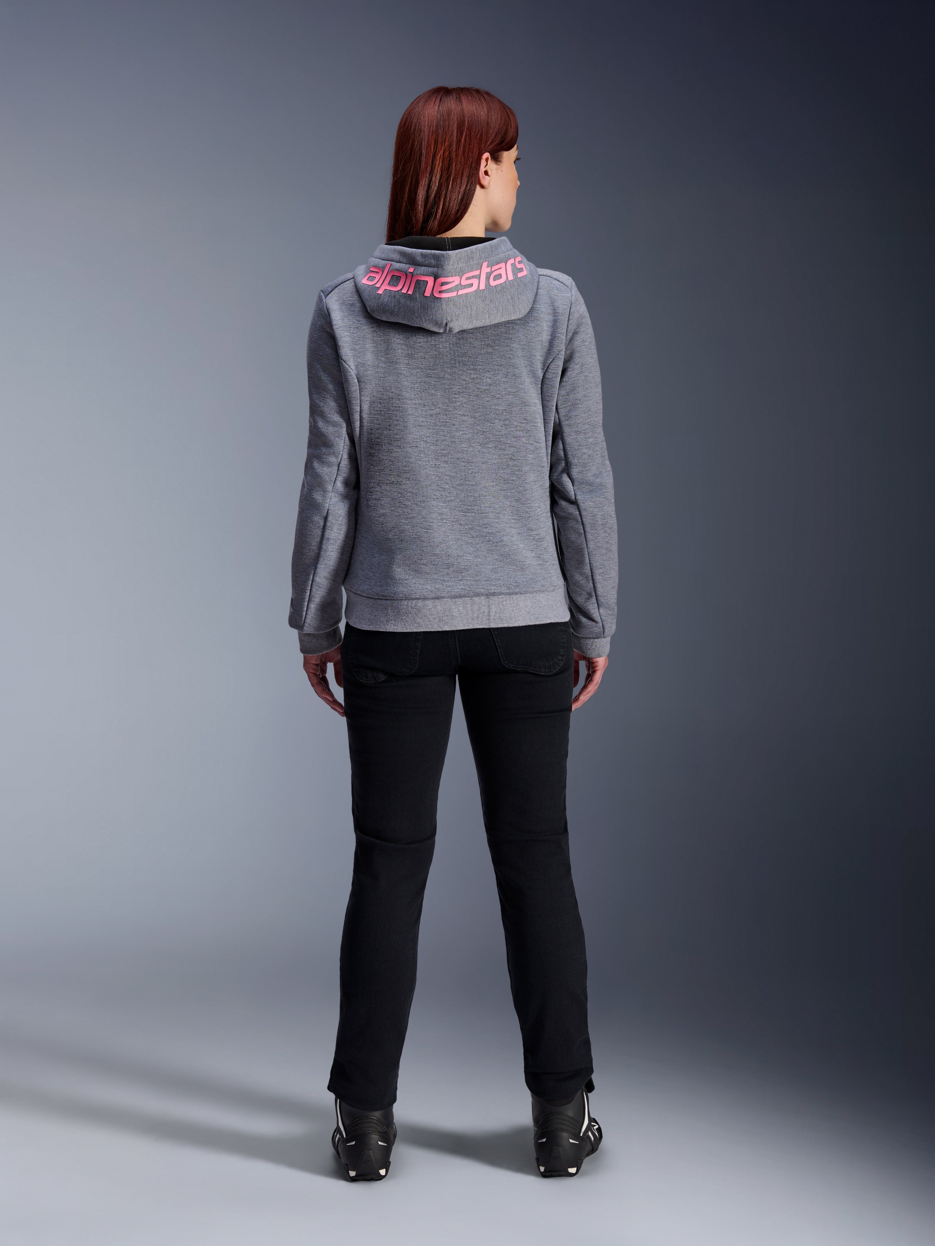 Alpinestars Stella Chrome V2 Sport Hoodie, felpa da moto da donna, grigio mélange e rosa fluo, vista posteriore con logo Alpinestars rosa sul cappuccio, indossata con pantaloni da guida e stivali neri, abbigliamento moto casual da donna