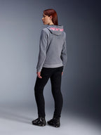 Alpinestars Stella Chrome V2 Sport Hoodie, felpa da moto da donna, grigio mélange con logo rosa fluo sul cappuccio, vista posteriore, abbinata a pantaloni neri e scarpe tecniche da guida, stile urban casual con protezione da moto