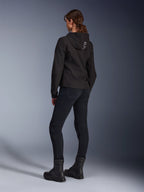 Alpinestars Stella Radium Tech Hoodie, felpa da moto urbana da donna nera, vista posteriore con logo 'ALPIN' sul cappuccio, abbinata a pantaloni tecnici da guida neri e stivali neri, guscio tecnico leggero antivento.
