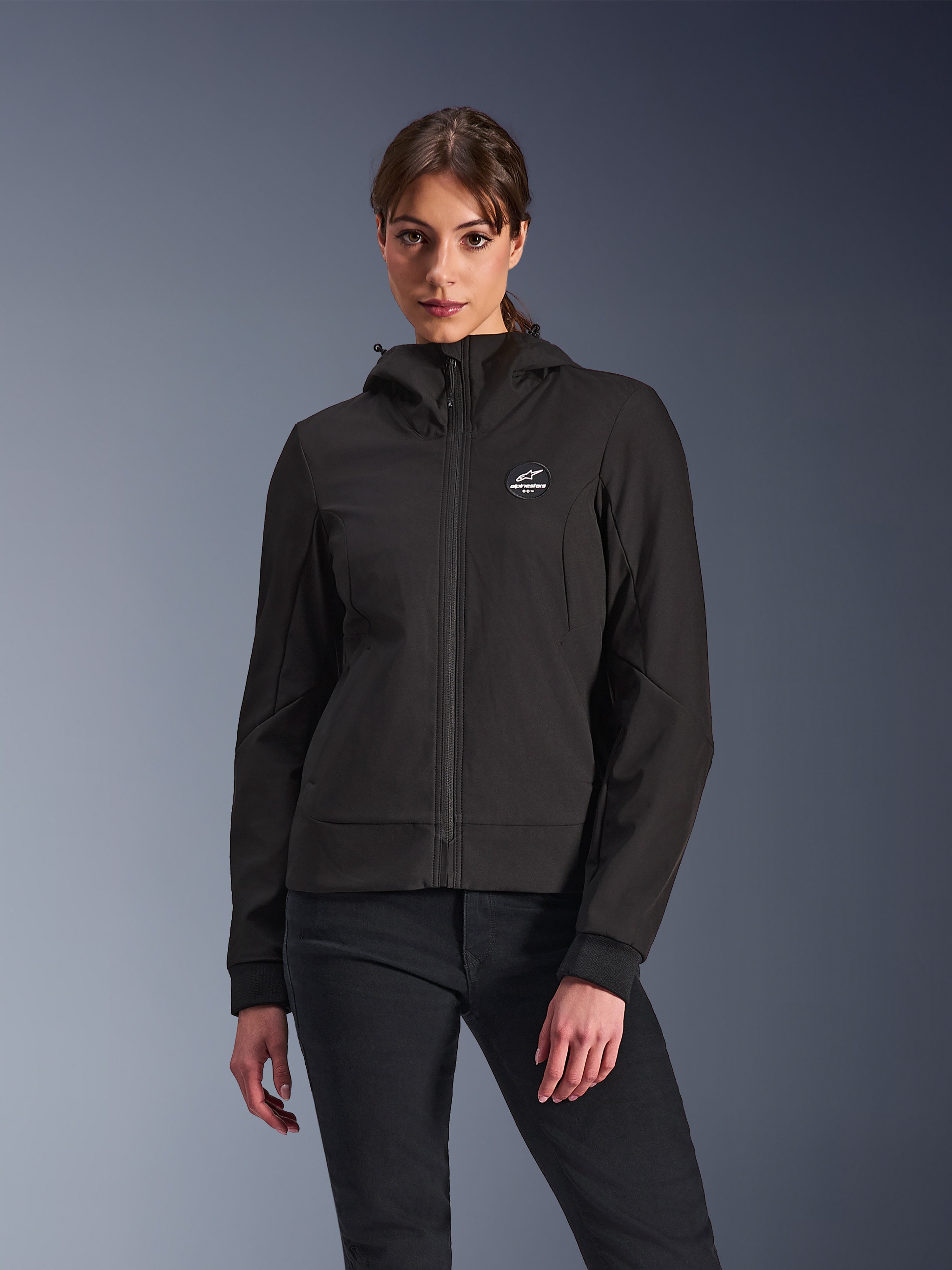 Alpinestars Stella Radium Tech Hoodie, felpa da moto da donna con cappuccio, nera, design con zip con logo circolare sul petto e cappuccio, abbigliamento tecnico per guida urbana, indossata da una modella