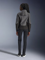 Donna che indossa la felpa Alpinestars Stella Radium Tech Hoodie, grigio scuro e nero, vista posteriore con marchio 'ALPIN' sul cappuccio, abbinata a pantaloni neri slim-fit e sneakers nere, abbigliamento da moto urbano