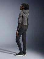 Donna che indossa la felpa con cappuccio Alpinestars Stella Radium Tech in Deep Gray e Black, abbigliamento moto urbano, vista posteriore che mostra il cappuccio con marchio Alpinestars, abbinata a pantaloni slim-fit neri e sneaker alte