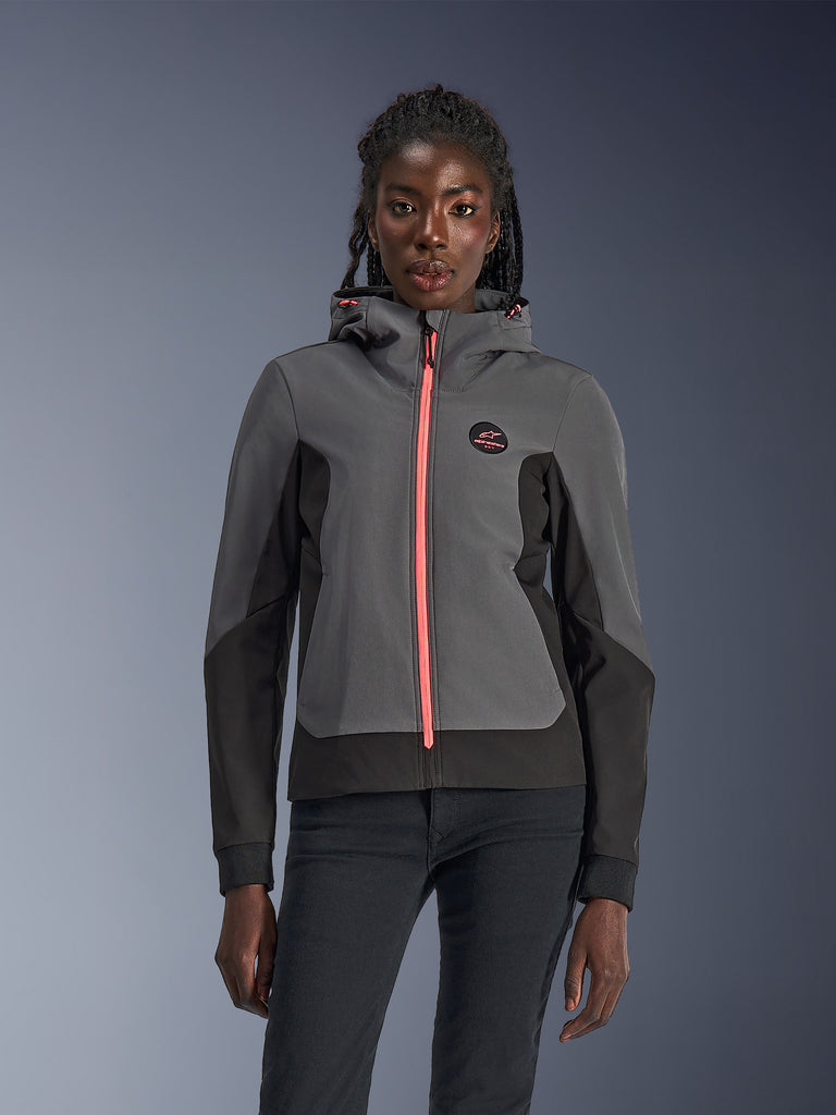 Alpinestars Stella Radium Tech Hoodie, felpa da moto da donna, grigio scuro e nero con zip e cordini del cappuccio rosa acceso, indossata da una modella, design urbano sportivo con logo Alpinestars sul petto
