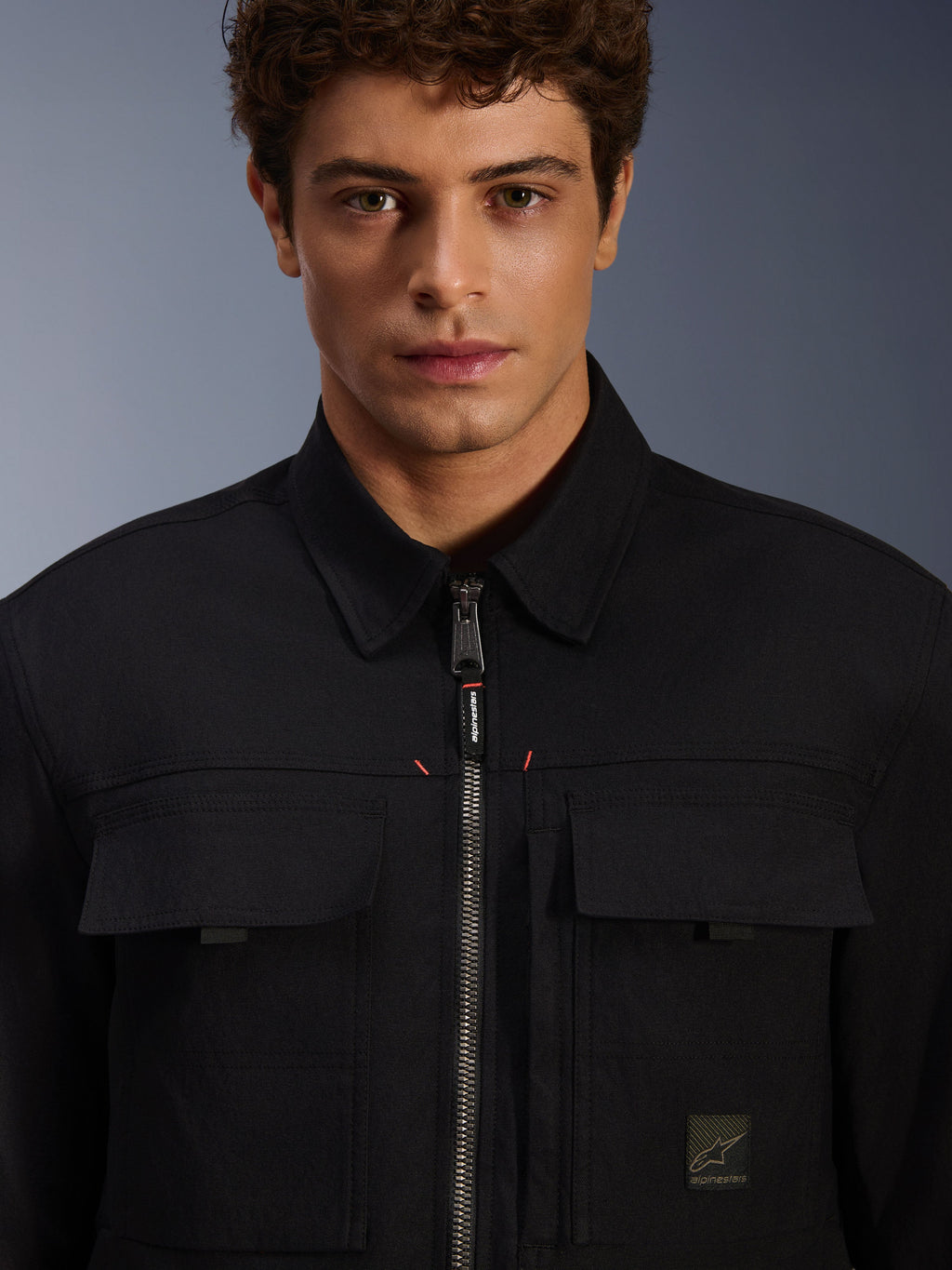 Alpinestars Bryon Water Resistant Overshirt, nero, vista ravvicinata della zip frontale e delle tasche sul petto, tessuto in canvas cerato resistente, design urbano minimalista con dettagli del brand ed etichetta logo tessuta