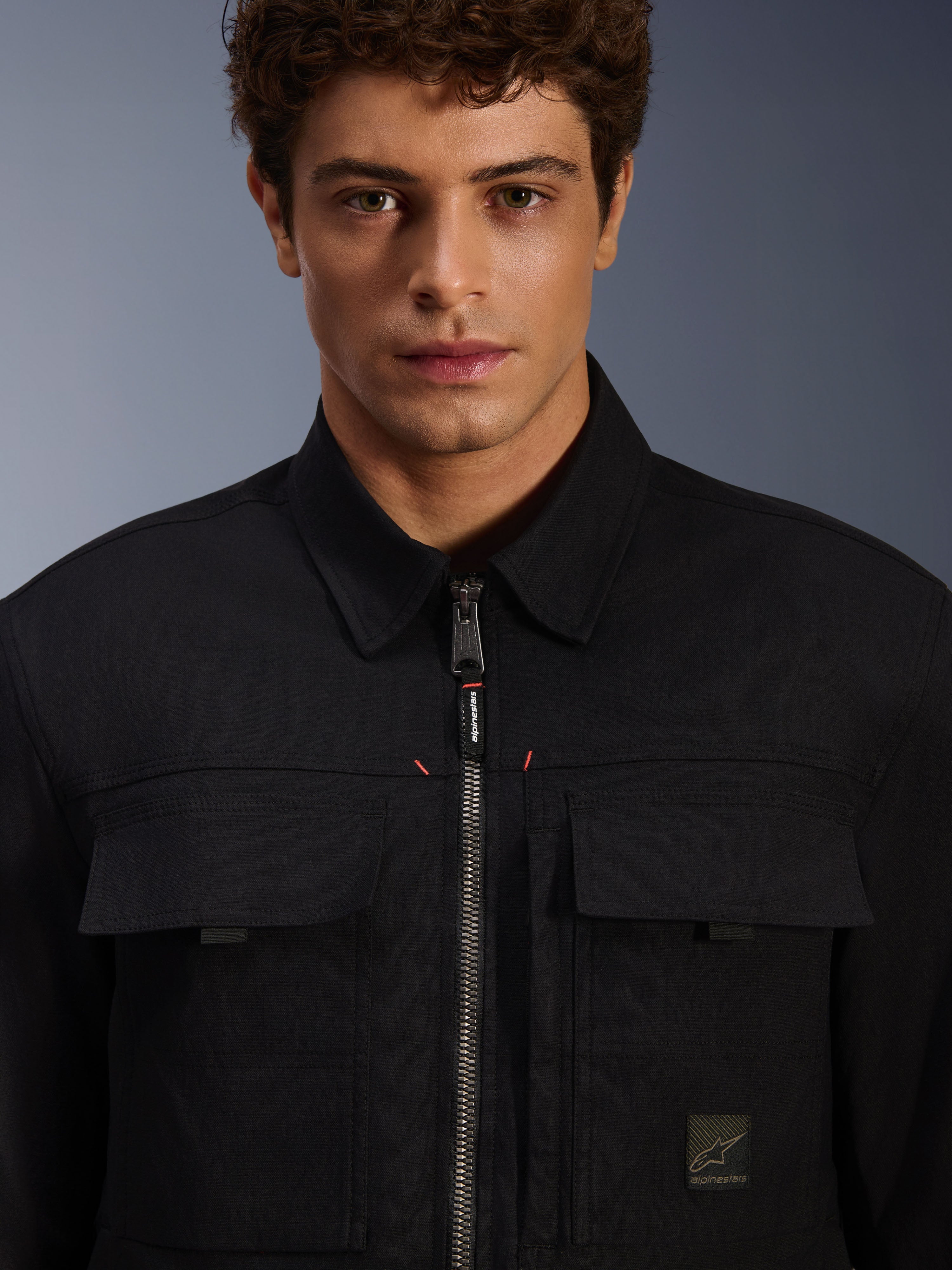 Alpinestars Bryon Water Resistant Overshirt, nero, vista ravvicinata della zip frontale e delle tasche sul petto, tessuto in canvas cerato resistente, design urbano minimalista con dettagli del brand ed etichetta logo tessuta