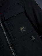 Alpinestars Bryon Water Resistant Overshirt, nero, vista ravvicinata del tessuto in tela cerata, cerniera frontale, tasca cargo sul petto con patch logo Alpinestars e dettaglio anello a D in metallo