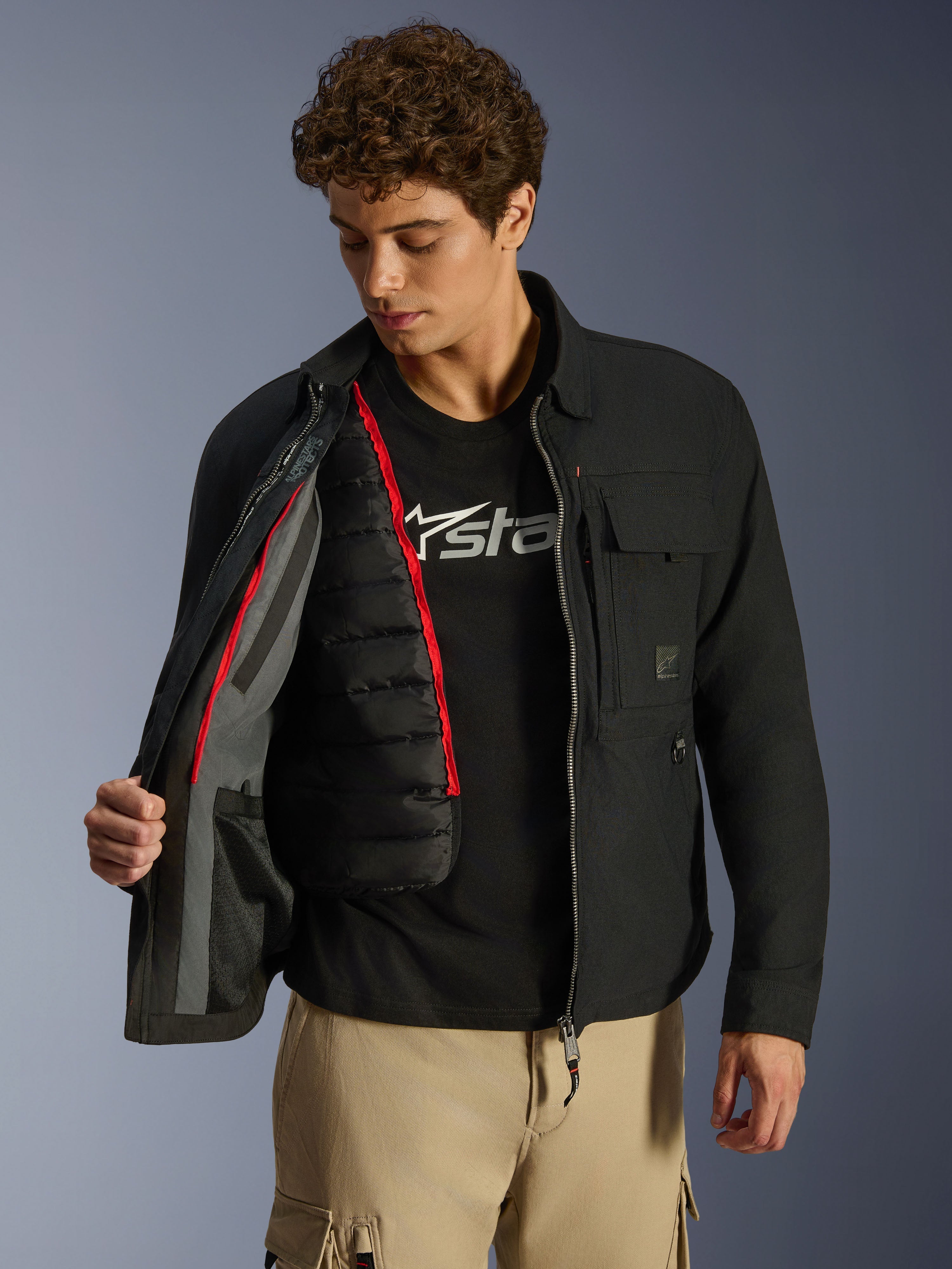 Alpinestars Bryon WR Overshirt, nero, giacca da moto urban mostrata aperta per rivelare un gilet termico trapuntato nero rimovibile con profili rossi, indossata con pantaloni cargo color sabbia e t-shirt con logo, design funzionale ispirato all'abbigliamento da lavoro