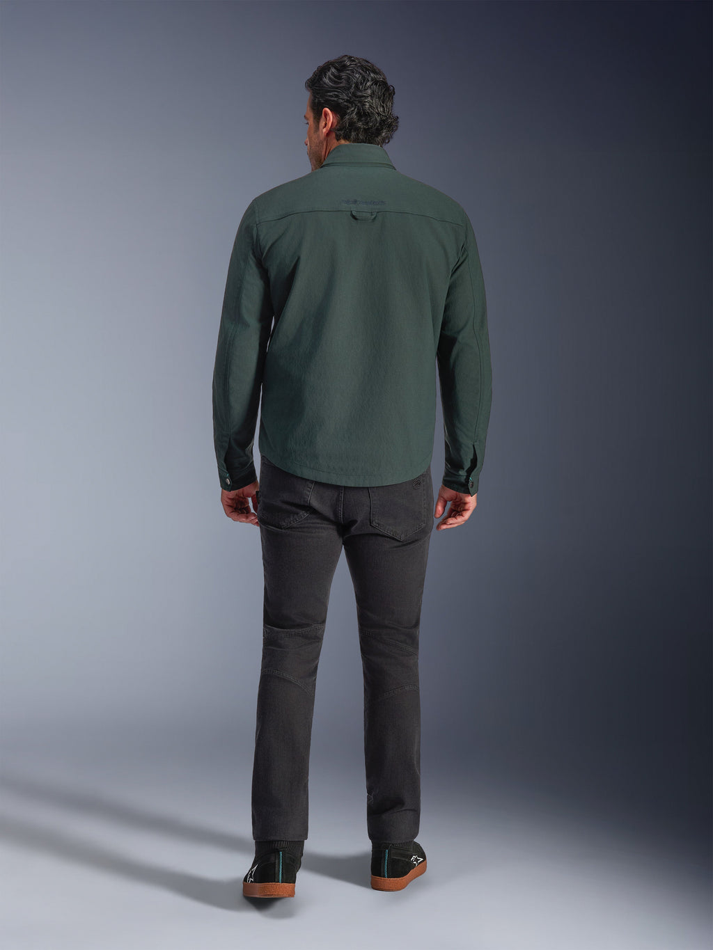 Alpinestars Bryon Water Resistant Overshirt in Dark Emerald, vista posteriore su modello, abbinata a pantaloni da moto grigio scuro e scarpe da guida nere, design classico ispirato all'abbigliamento da lavoro con retro leggermente più lungo per maggiore copertura durante la guida
