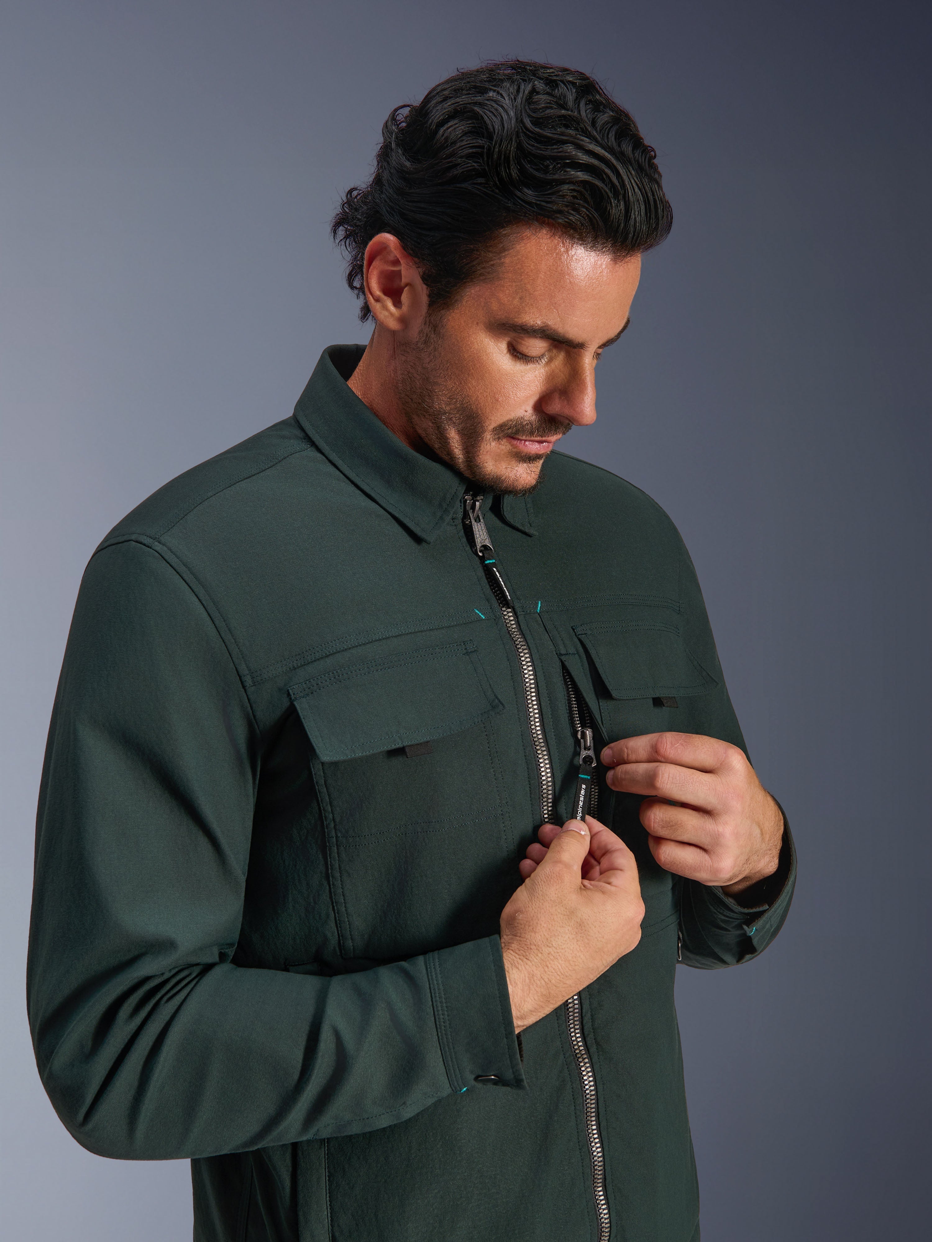Alpinestars Bryon WR Overshirt in Dark Emerald, giacca da moto urban, indossata da un uomo che mostra la tasca sul petto con cerniera verticale e le tasche cargo, caratterizzata da una resistente trama in tela cerata e un design ispirato all'abbigliamento da lavoro.