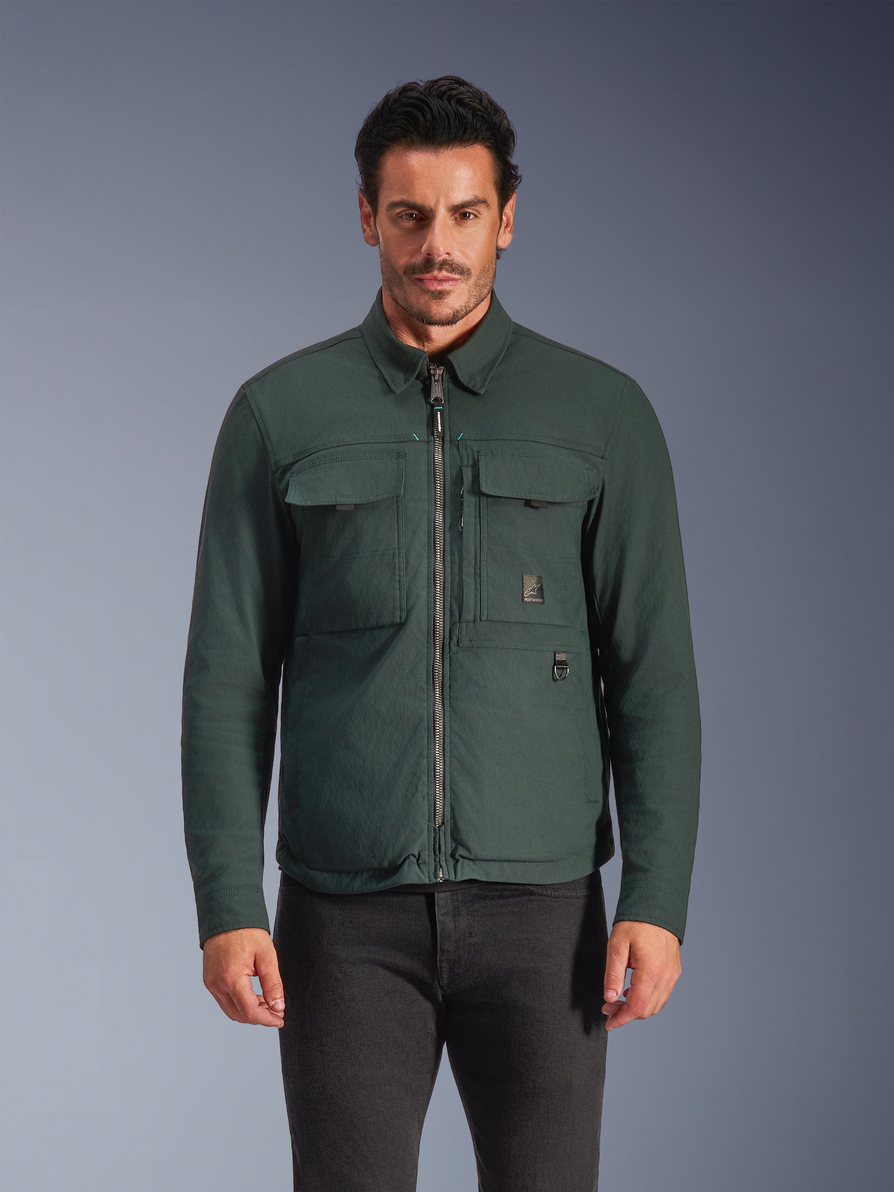 Alpinestars Bryon Water Resistant Overshirt, Dark Emerald, giacca da moto urban da uomo, modello che indossa una overshirt verde scuro con cerniera frontale e ampie tasche cargo sul petto, tela cerata resistente all'acqua per la guida su strada in moto