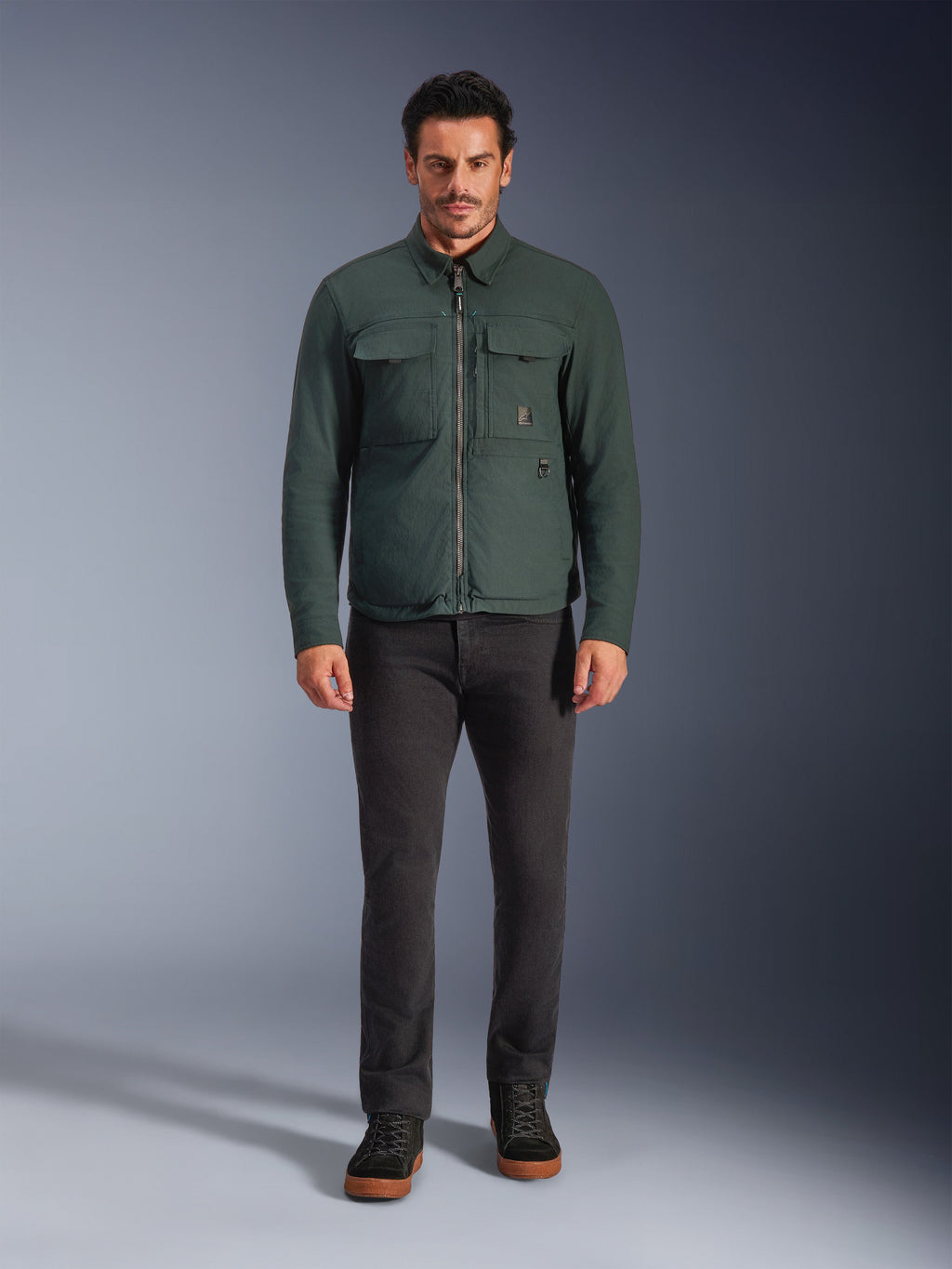 Alpinestars Bryon WR Overshirt, giacca da moto resistente all'acqua, smeraldo scuro, indossata con pantaloni neri e stivali neri, caratterizzata da una costruzione in tela cerata, tasche cargo sul petto e un design urbano moderno.