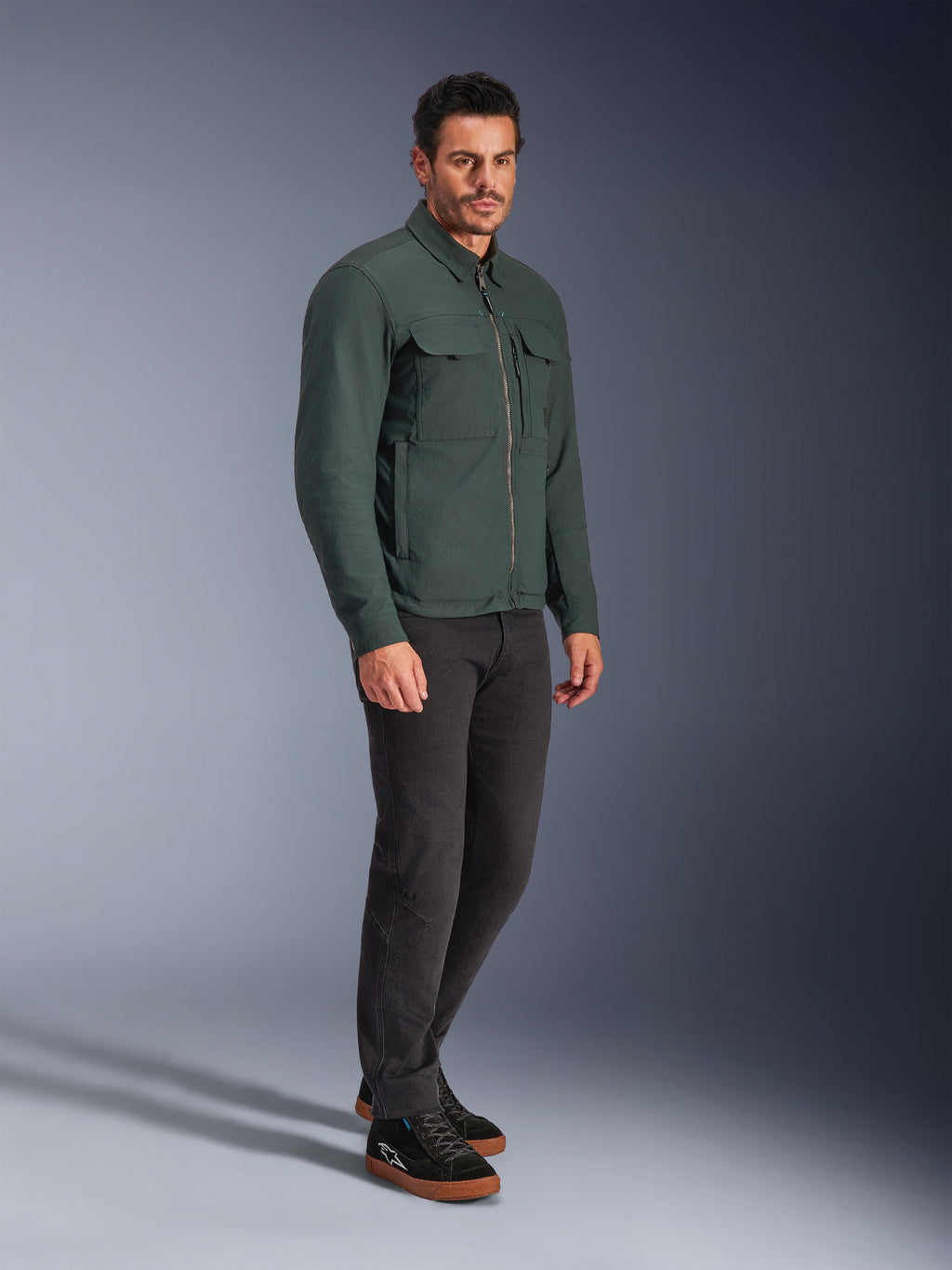 Alpinestars Bryon WR Overshirt, giacca da moto in Dark Emerald, tela cerata resistente all'acqua con tasche cargo sul petto e zip frontale, indossata da un modello con pantaloni scuri e sneaker nere, abbigliamento tecnico urban contemporary