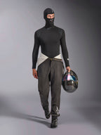 Passamontagna Alpinestars ZX Evo V3, nero, indossato da un modello con un completo base layer da corsa coordinato, maglia a maniche lunghe e pantaloni grigi, mentre tiene un casco in fibra di carbonio con visiera iridescente, equipaggiamento professionale per corse automobilistiche