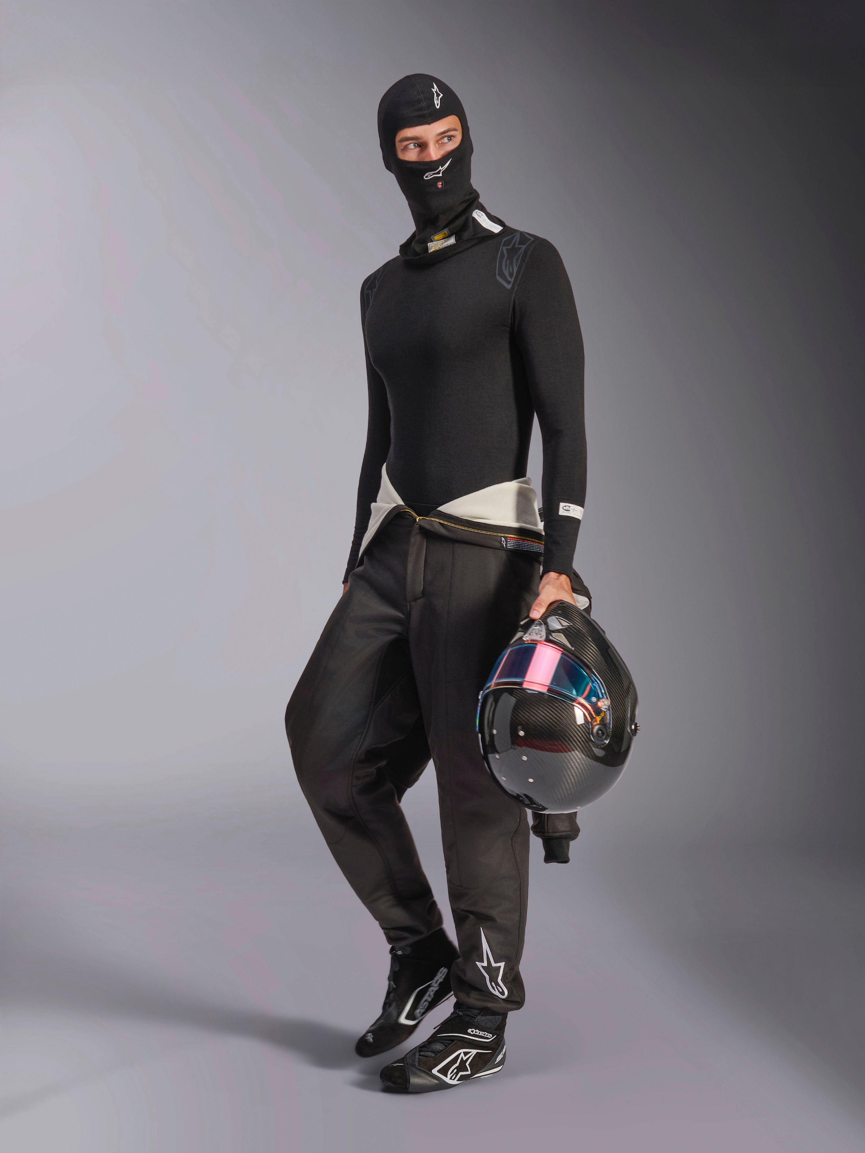 Passamontagna Alpinestars ZX Evo V3, nero, indossato da un pilota con abbigliamento intimo da corsa completo, logo bianco sulla fronte, con casco in fibra di carbonio e visiera iridescente, abbigliamento professionale ignifugo per motorsport.