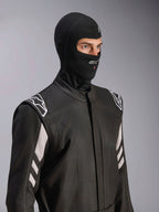 Alpinestars ZX Evo V3 Balaclava, nero, passamontagna ignifugo per corse automobilistiche, indossato da un modello in tuta da corsa nera con accenti bianchi, logo Alpinestars sul mento, apertura per il tubo di idratazione, equipaggiamento protettivo professionale per motorsport
