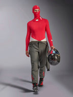 Alpinestars ZX Evo V3 Balaclava in rosso, indossato da un pilota con base layer a maniche lunghe coordinato e pantaloni da corsa grigi, con in mano un casco in fibra di carbonio, abbigliamento professionale ignifugo per auto da corsa