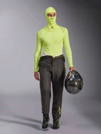 Alpinestars ZX Evo V3 Balaclava in Yellow Fluo, indossato con maglia base layer a maniche lunghe coordinata e pantaloni da corsa grigio scuro, modello maschile con in mano un casco in fibra di carbonio, attrezzatura professionale per corse automobilistiche