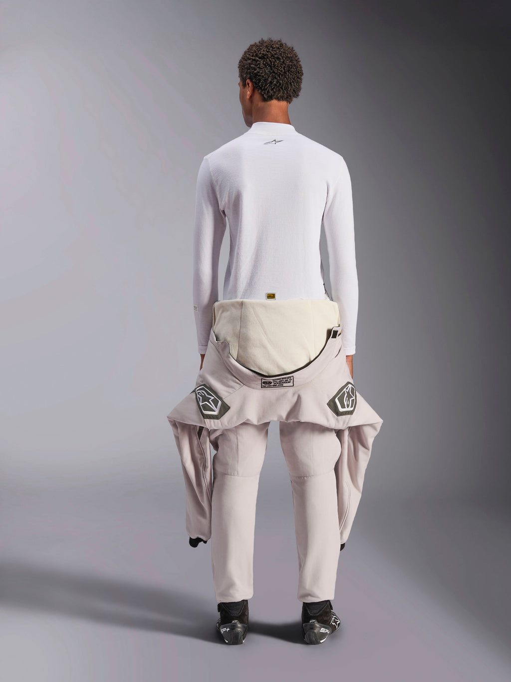 Alpinestars ZX Evo V3 Top - Long Sleeve, sottotuta bianco per corse automobilistiche, vista posteriore di una persona che indossa la maglia ignifuga con una tuta da gara abbassata in vita, abbinata a stivali da corsa neri, intimo tecnico professionale per motorsport