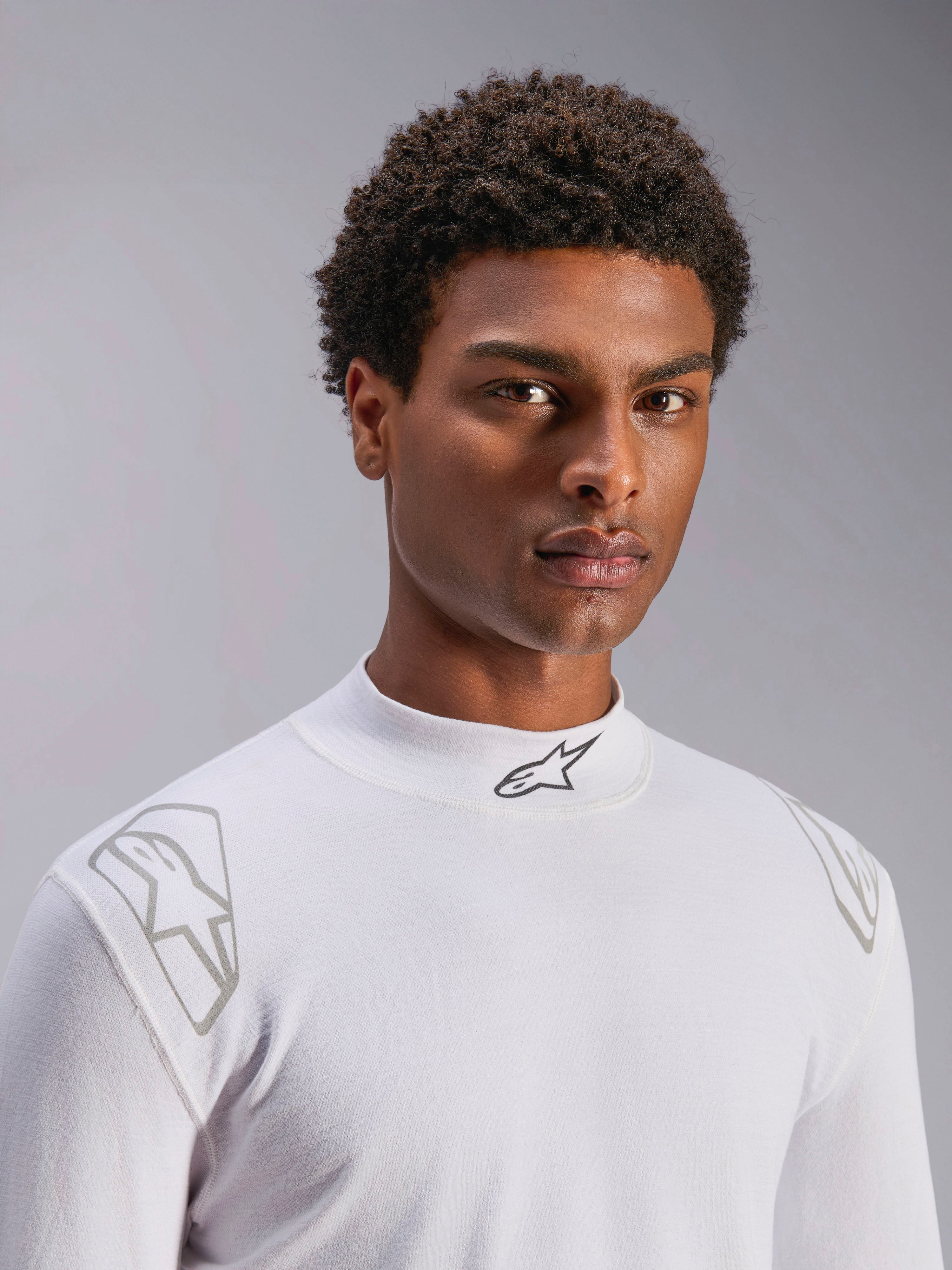 Alpinestars ZX Evo V3 Top - Manica Lunga, sottotuta bianco per auto racing, indossato da un modello, collo a lupetto con logo Alpinestars nero, stampe grafiche argentate sulle spalle, intimo da motorsport leggero e resistente alle fiamme