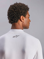 Alpinestars ZX Evo V3 Top, sottotuta auto a maniche lunghe, bianco, primo piano della zona posteriore del collo con logo Alpinestars nero, tessuto tecnico resistente alle fiamme, indossata da un modello con capelli scuri e ricci