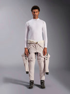 Alpinestars ZX Evo V3 Top, a maniche lunghe, bianco, base layer per corse automobilistiche indossato con una tuta da gara chiara legata in vita e stivali da corsa neri, con collo a lupetto con logo e branding sulle spalle, intimo professionale ignifugo per motorsport
