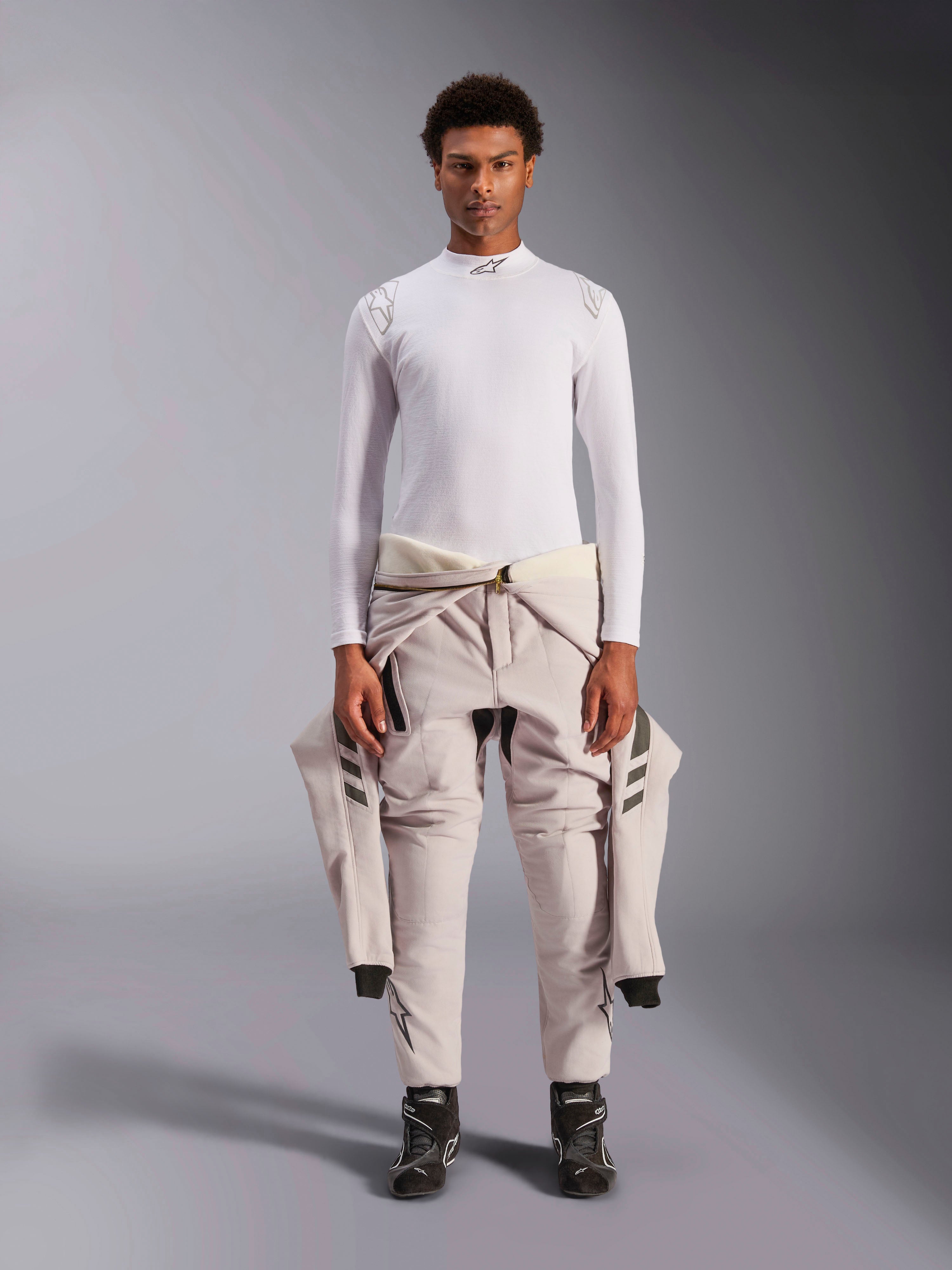 Alpinestars ZX Evo V3 Top, a maniche lunghe, bianco, base layer per corse automobilistiche indossato con una tuta da gara chiara legata in vita e stivali da corsa neri, con collo a lupetto con logo e branding sulle spalle, intimo professionale ignifugo per motorsport
