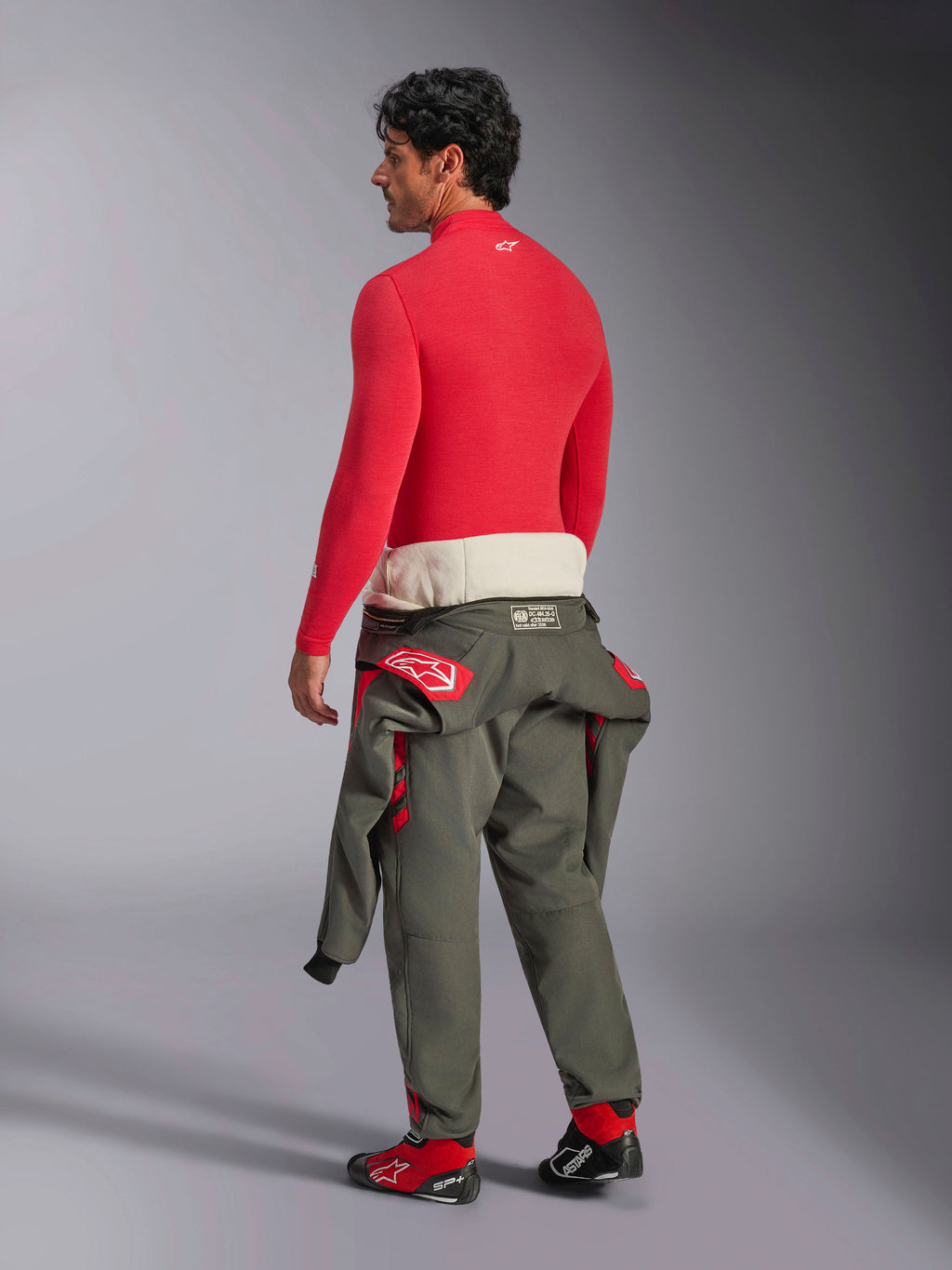 Alpinestars ZX Evo V3 Long Sleeve Top, base layer auto rosso, vista posteriore su modello maschile che indossa pantaloni della tuta da gara verde oliva in vita e scarpe da corsa rosse, intimo tecnico resistente alle fiamme per il motorsport