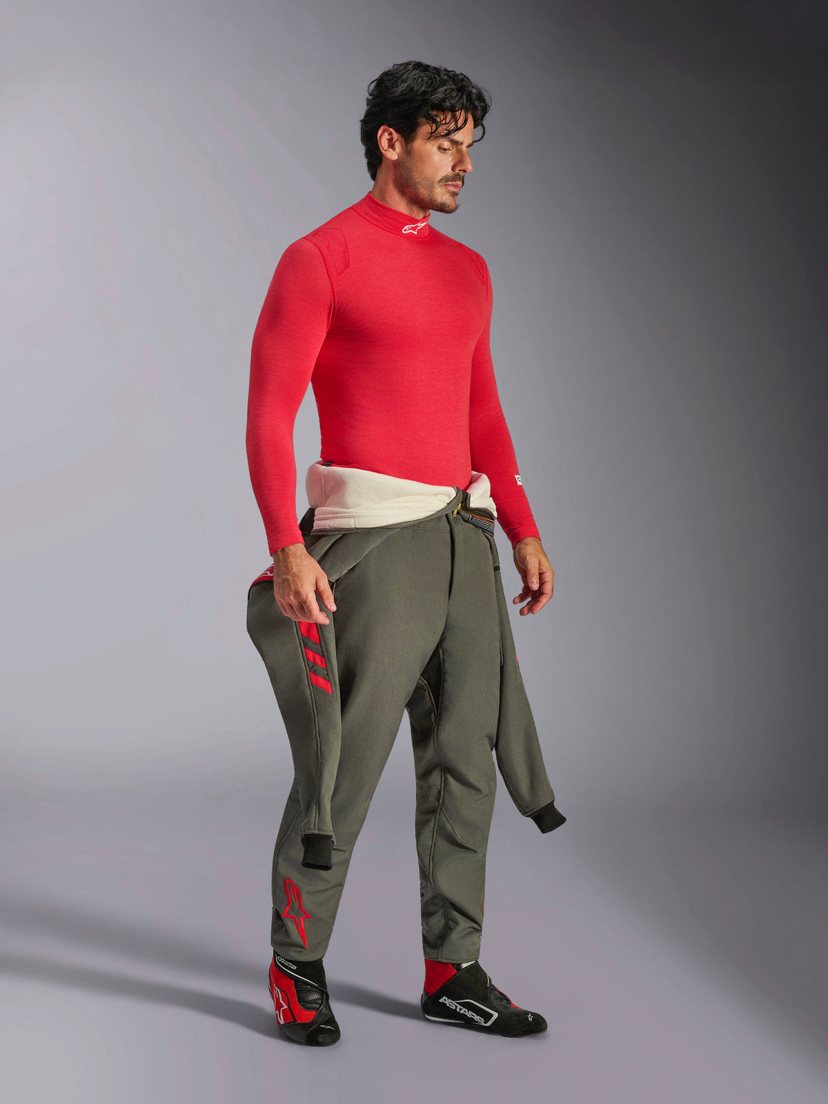 Alpinestars ZX Evo V3 Top a maniche lunghe in rosso, sottotuta ignifugo per corse automobilistiche, indossato con pantaloni da corsa verde oliva e scarpe da corsa nere e rosse, equipaggiamento professionale per motorsport, ritratto in studio