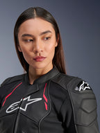 Donna che indossa la giacca in pelle Alpinestars Stella Dusk in Black Diva Pink White, con logo bianco sul petto, vivaci accenti rosa e protezione esterna per le spalle DFS, abbigliamento da moto in pregiata pelle bovina
