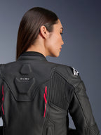 Donna che indossa la giacca in pelle Alpinestars Stella Dusk, pelle nera con accenti Diva Pink e logo bianco sulla spalla, vista posteriore con marchio DUSK e pannelli elasticizzati a fisarmonica, design ergonomico sportivo
