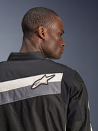 Giacca Alpinestars T-Dyno WR, giacca da moto in tessuto, nero, grigio scuro ed ecru, primo piano della parte superiore della schiena e della spalla con strisce orizzontali e logo a stella Alpinestars, indossata da un modello, design di ispirazione heritage per la guida su strada