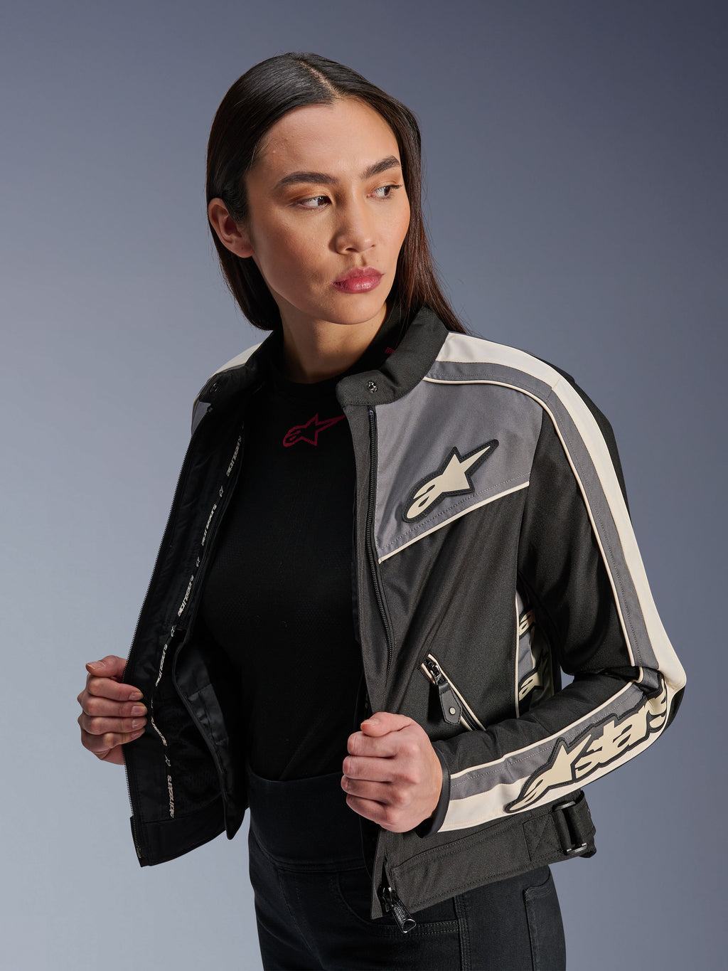 Giacca Alpinestars Stella T-Dyno WR da donna, giacca da moto in tessuto, nero, grigio scuro ed ecru, design d'ispirazione vintage con strisce sportive e loghi su petto e maniche, indossata da una modella, abbigliamento per guida su strada urbana