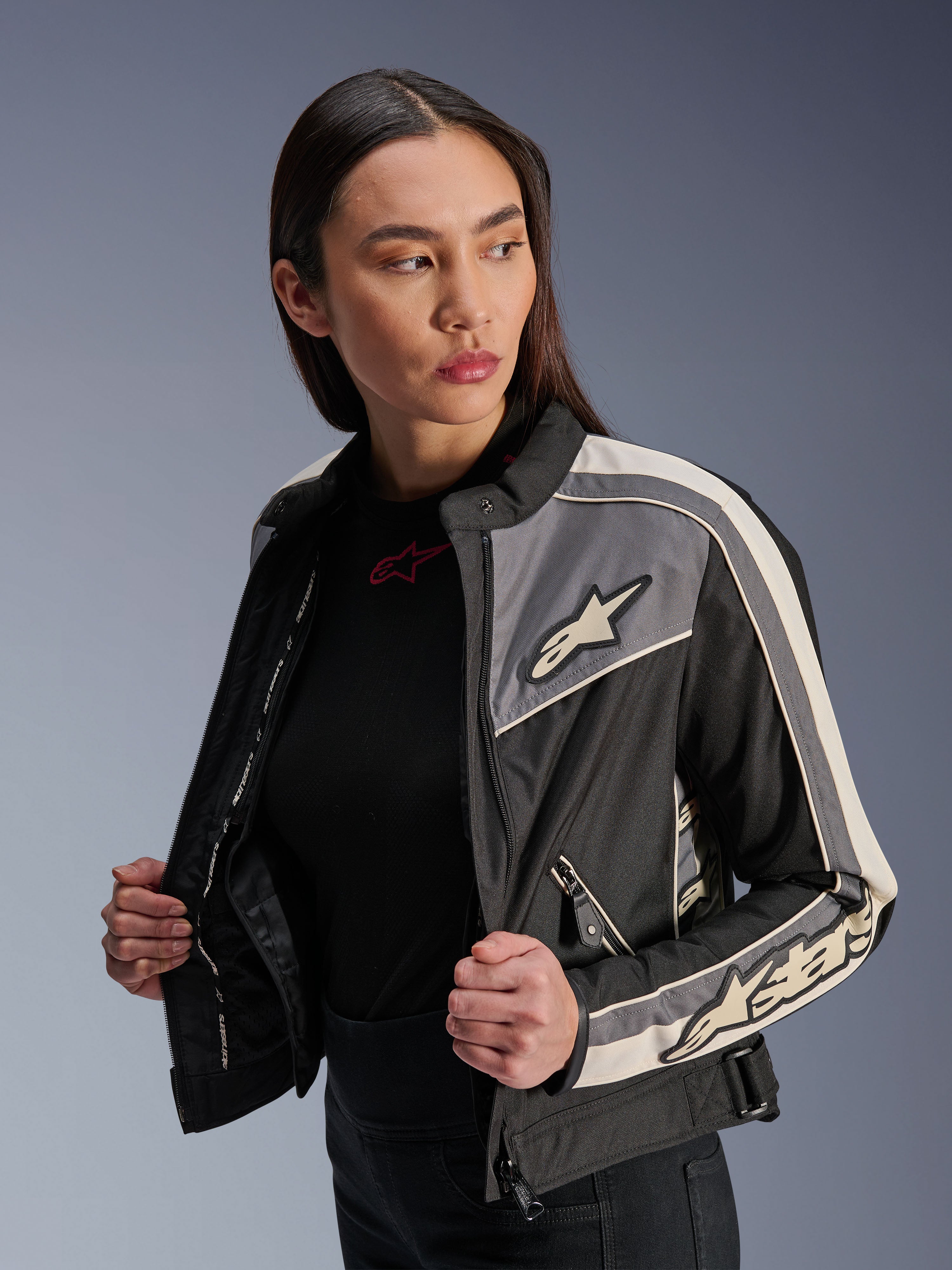 Giacca Alpinestars Stella T-Dyno WR da donna, giacca da moto in tessuto, nero, grigio scuro ed ecru, design d'ispirazione vintage con strisce sportive e loghi su petto e maniche, indossata da una modella, abbigliamento per guida su strada urbana