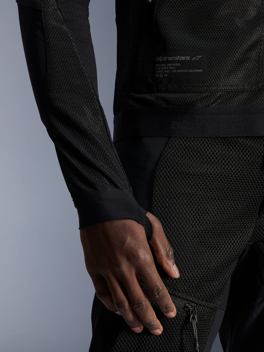 Alpinestars Troop-Air Jacket, nero, primo piano della costruzione in mesh tecnico, patch logata con testo tecnico e manica con passante per il pollice integrato, giacca da moto urbana estiva ad alto flusso d'aria