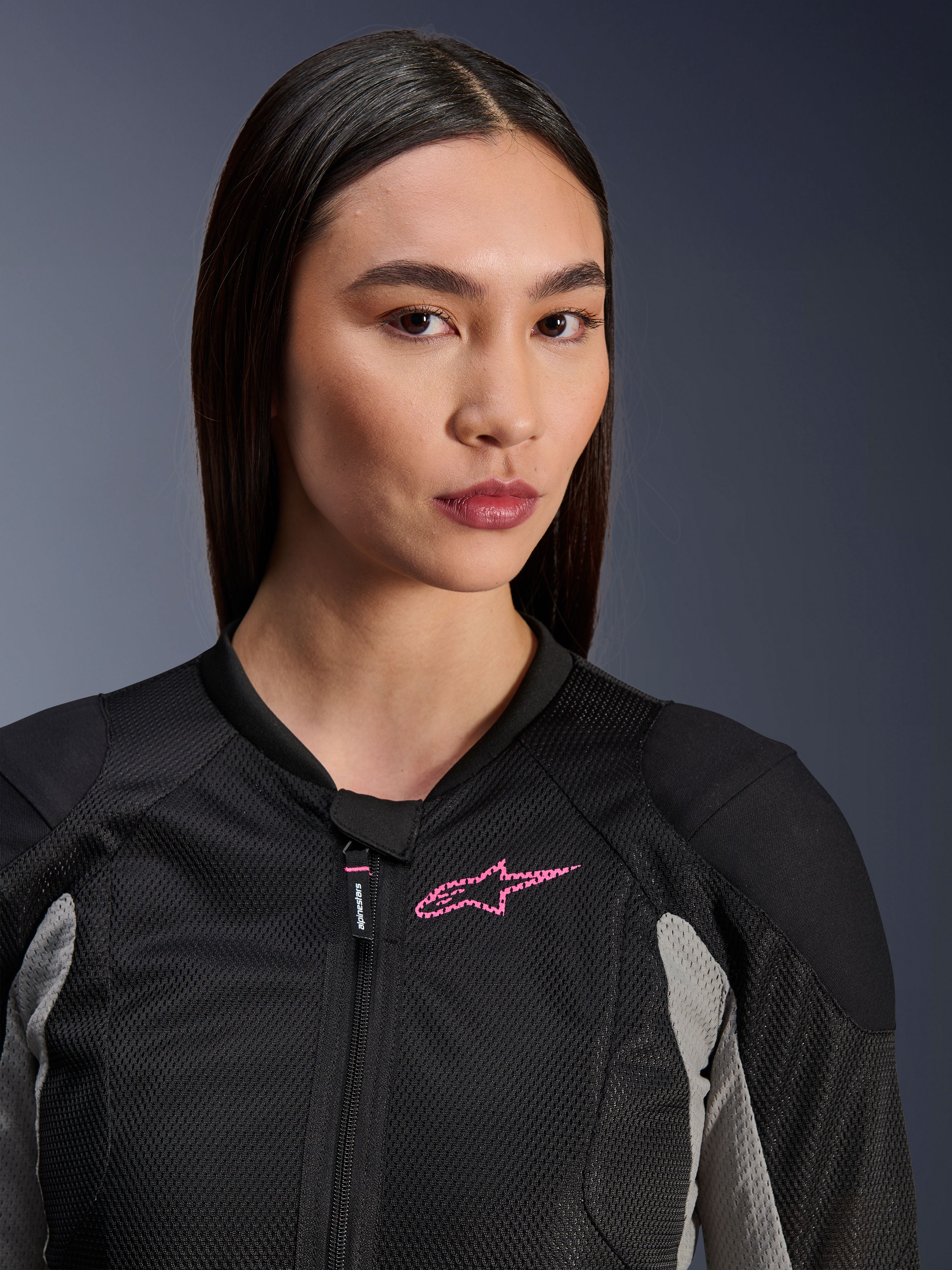 Donna che indossa la giacca Alpinestars Stella Troop-Air, Nero, Grigio Cenere e Rosa Fluo, vista ravvicinata che mette in risalto la costruzione in mesh tecnico e il logo rosa sul petto, abbigliamento da moto urbano di stile