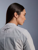 Donna che indossa la giacca Alpinestars Stella C-1 Air in argento, vista ravvicinata laterale-posteriore che mostra il logo Alpinestars nero, pannelli di ventilazione in rete tecnica e un design motociclistico urbano pulito e contemporaneo.