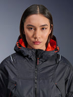 Alpinestars Giacca Molly Air, giacca da moto da donna, nero e corallo fluo, vista frontale ravvicinata su una modella, tessuto ripstop con ventilazione traforata al laser, fodera del cappuccio in rete arancione vivace e cordini, con branding delle protezioni Nucleon Flex Plus